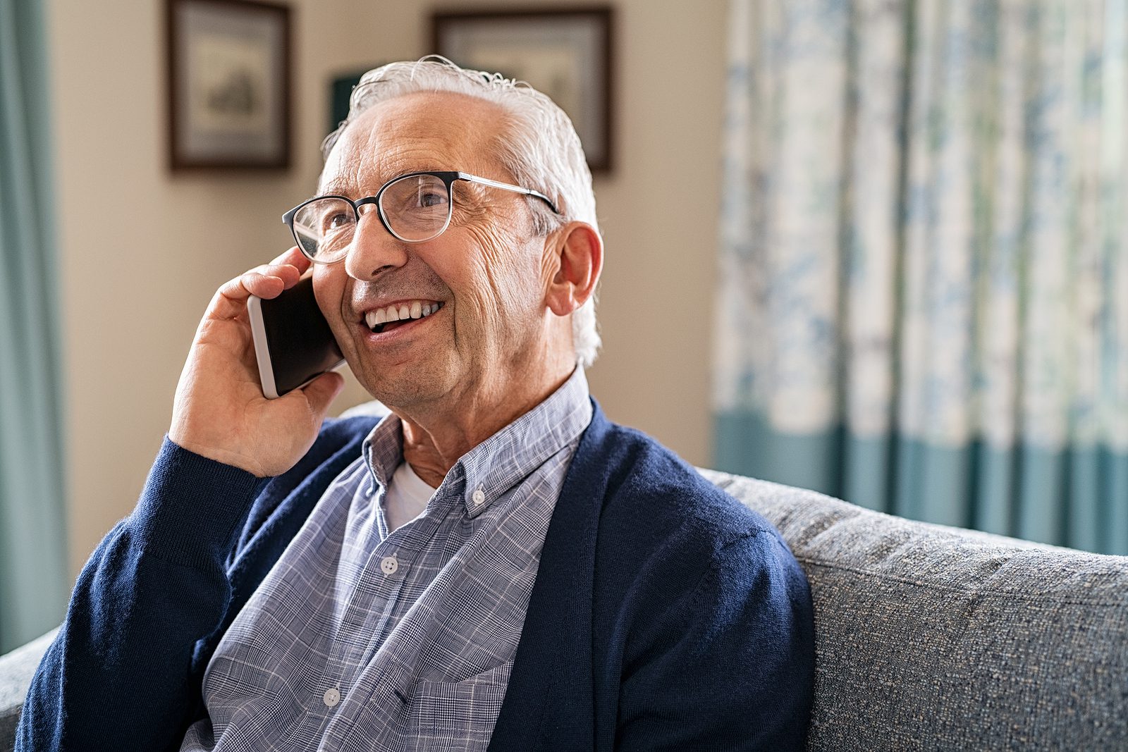 Smiling old man talking over smartphone while relaxing at home. Senior man after retirement using smart phone to connect with friends and family. Carefree elder talking over phone with her daughter.