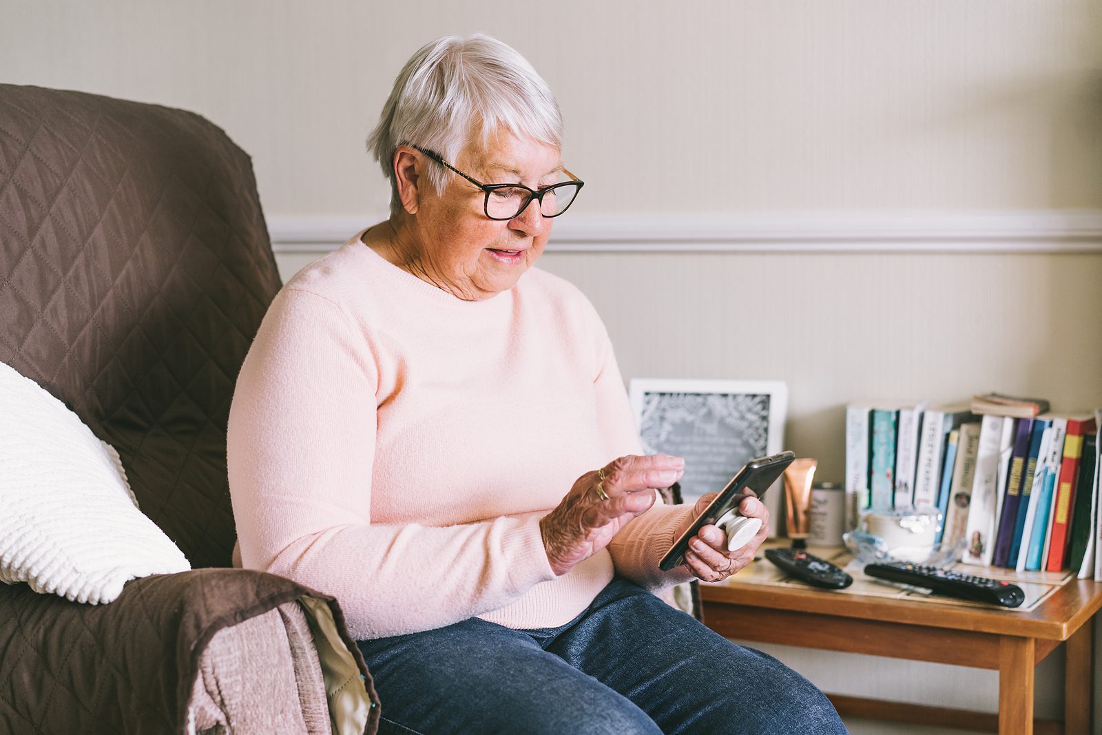 Senior woman using smartphone sitting on armchair at home. Relaxed mature older lady holding mobile phone texting, buying online, playing games, checking apps on cellphone. Seniors and technology
