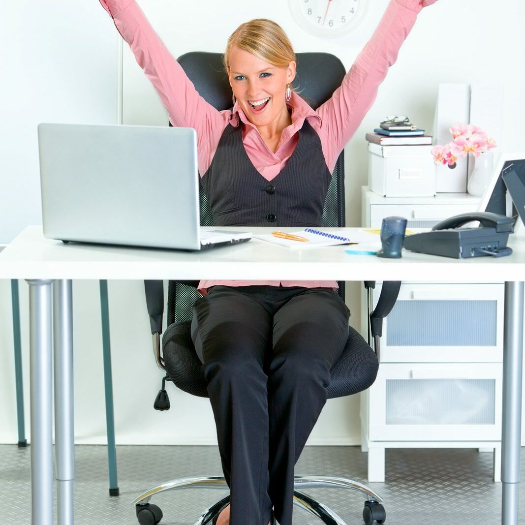 Excited modern business woman sitting at office desk and rejoicing her success